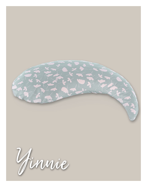 Ein bananenförmiges Kissen mit hellblauem Bezug und rosa Blumenmuster ruht auf einem beigen Hintergrund. Unten links steht der Schriftzug 